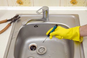 Close-up of handsome plumber repairing drain of kitchen sink. Photo of metalic sink and handyman with screwdriver in Thonotosassa, FL