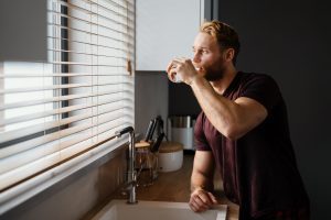 Smiling man drinking water from a glass while standing at the kitchen sink in Plant City, FL